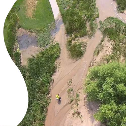 Aerial view of a person walking on a muddy path by a waterway amidst greenery.