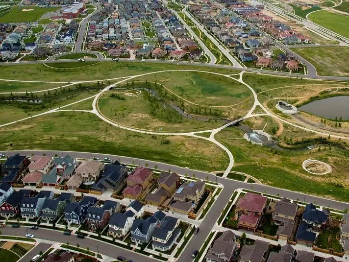 Aerial view of a suburban neighborhood with houses, streets, and a park with walking paths.