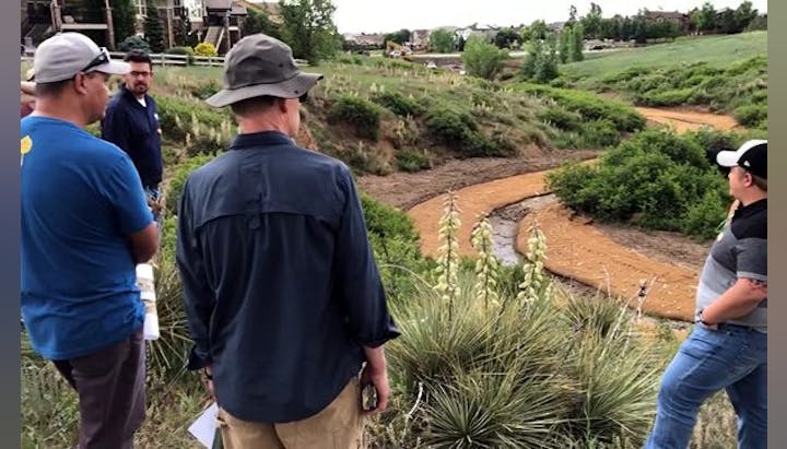 Group of people observing a water stream and erosion control landforms.
