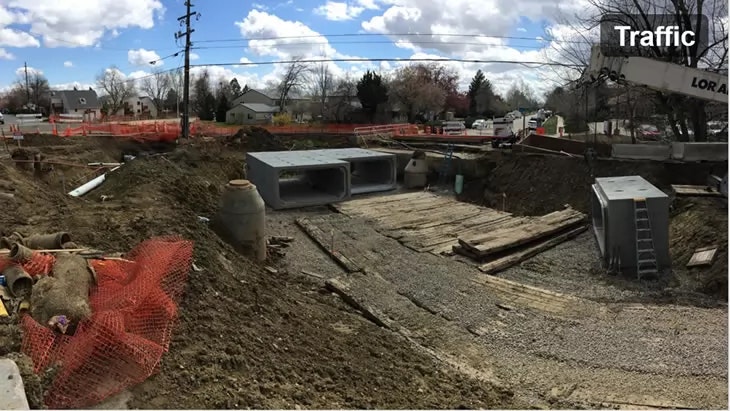 A construction site with a crane, concrete structures, excavation, and safety fences under a cloudy sky.