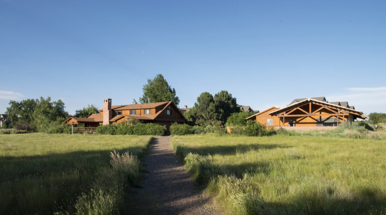 Rustic wooden buildings amidst grassy fields with a clear sky overhead.