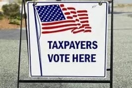 A sign that reads "TAXPAYERS VOTE HERE" with an American flag.