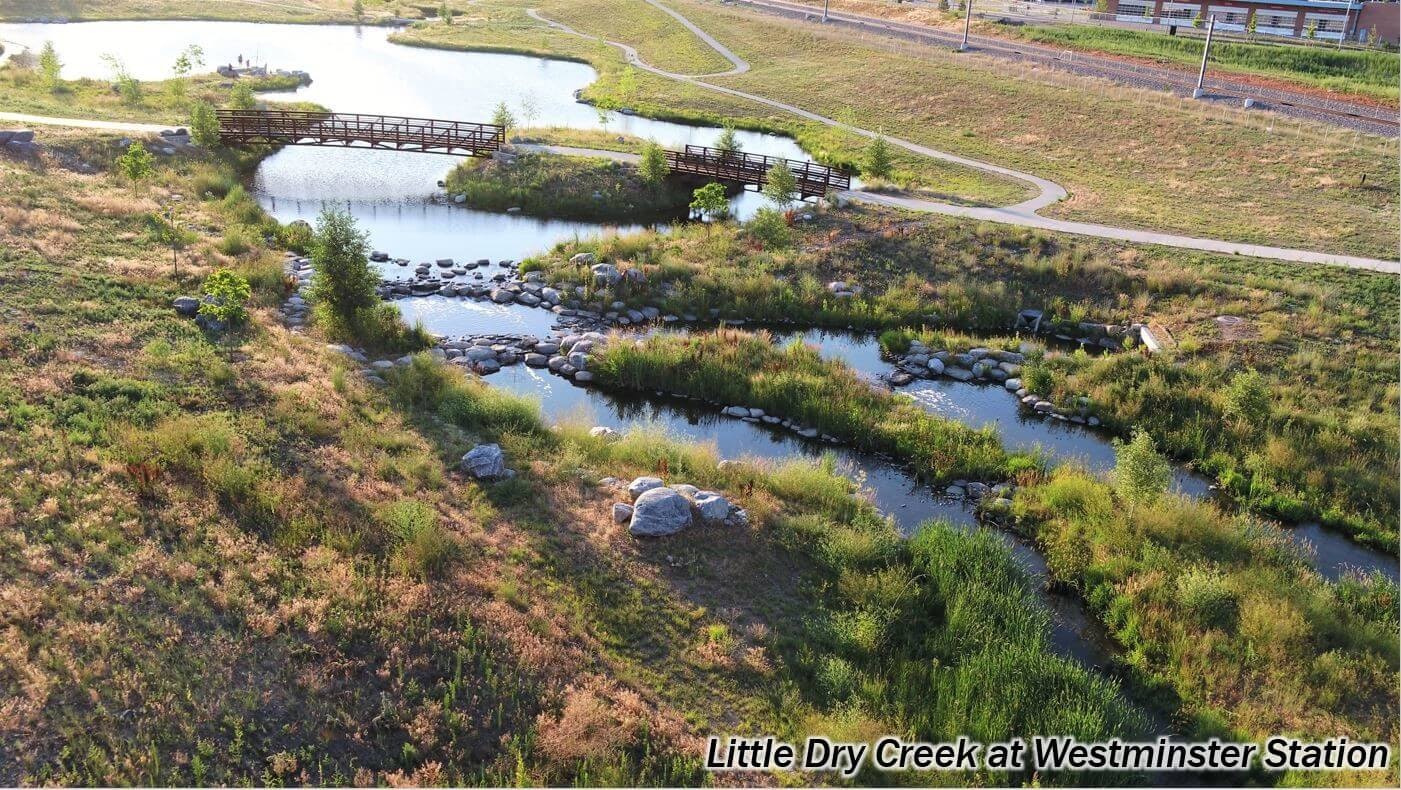 A creek with a footbridge surrounded by greenery and rocks, labeled "Little Dry Creek at Westminster Station."