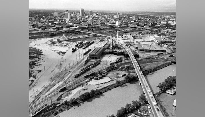 Aerial view of a cityscape with train tracks, roads, buildings, and a river.