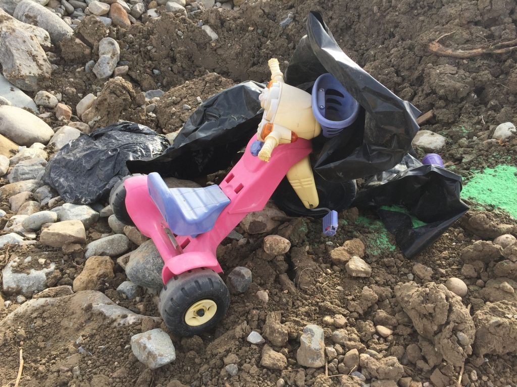 Discarded pink toy scooter amidst rubble and trash bags.