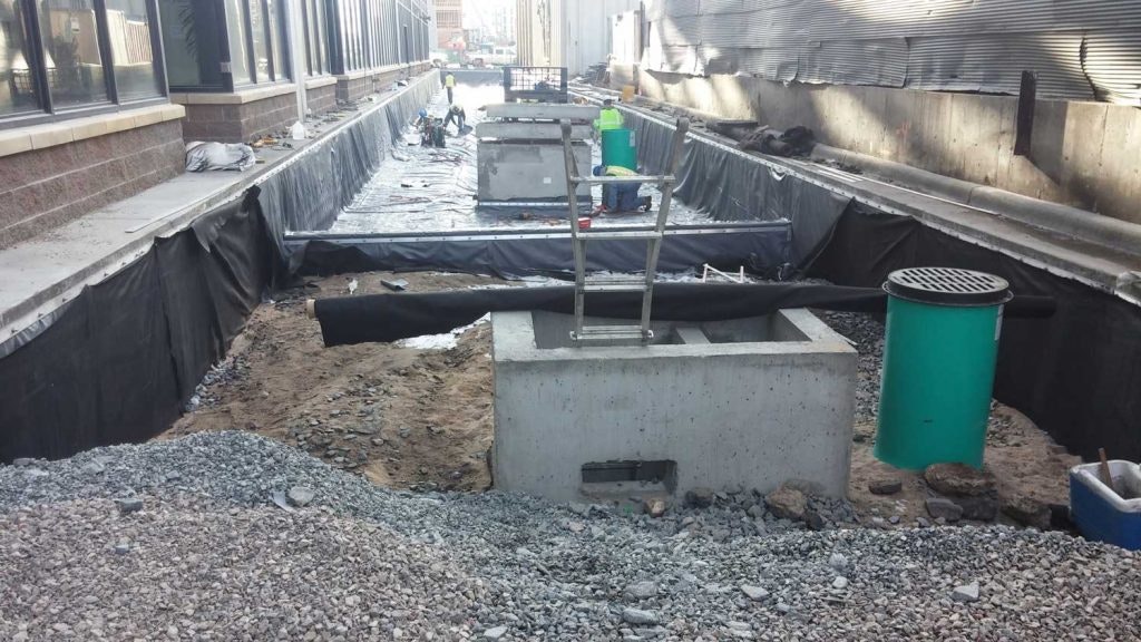 Construction site with trench, concrete structures, and a green trash bin.