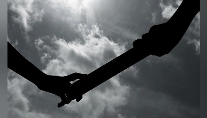 Two silhouetted hands almost touching, clouds and sun in the background.