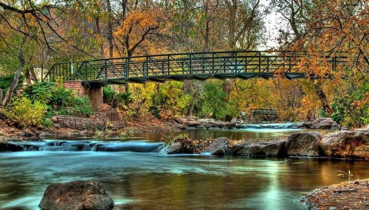 A serene stream with a metal bridge and autumn foliage.