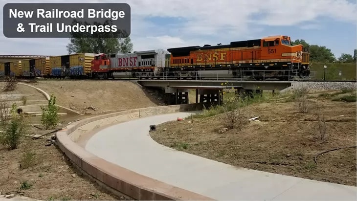 A new railroad bridge with a train on it and a trail underpass below.