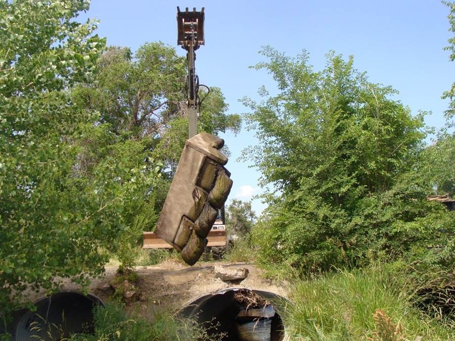 Heavy machinery lifting an oversized sofa in a green, overgrown area.