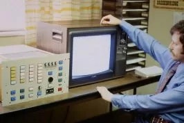 A person with vintage computer equipment, including a monitor and control panel.