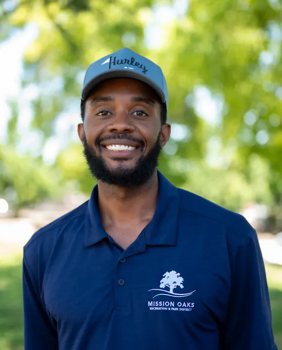 A smiling man wearing a cap and a blue polo with "Mission Oaks Recreation & Park District" logo, set in a green outdoor background.