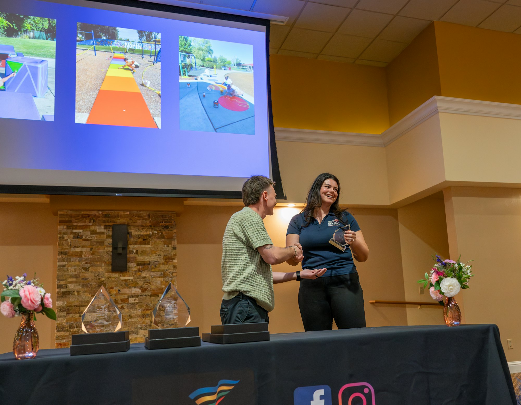 A presentation event featuring a woman receiving an award, with images of playgrounds displayed on a screen.