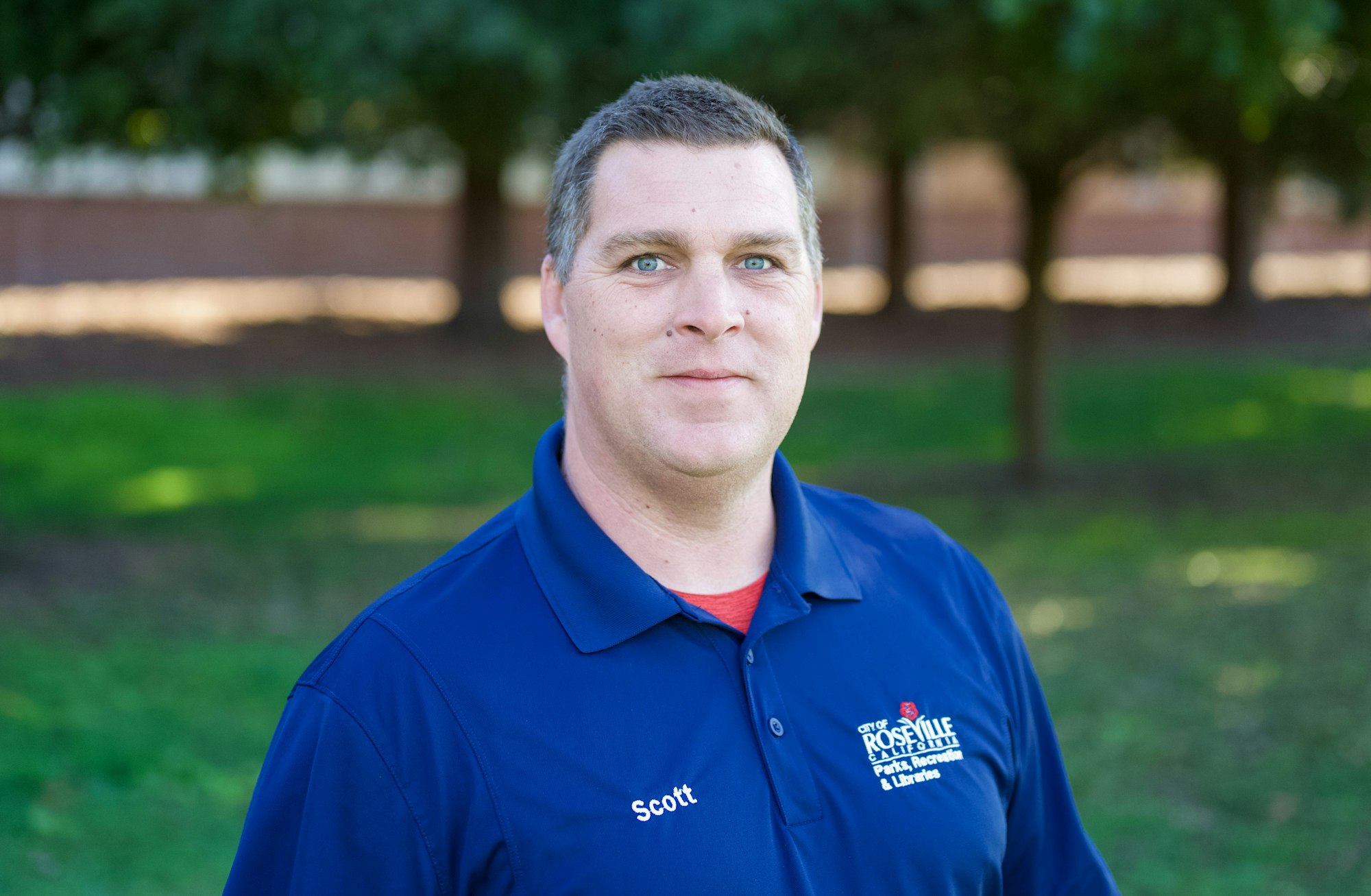 A person in a "Roseville Parks, Recreation & Libraries" blue shirt stands outdoors.