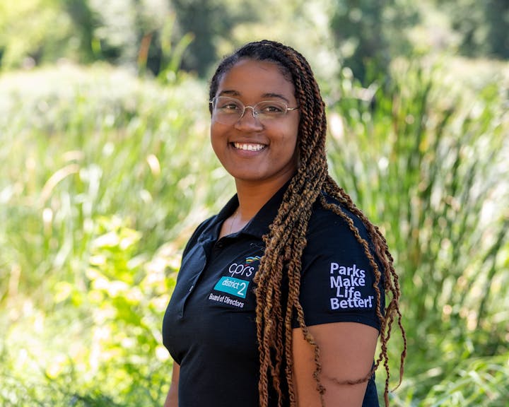 Person smiling outdoors, wearing a "Parks Make Life Better!" shirt.