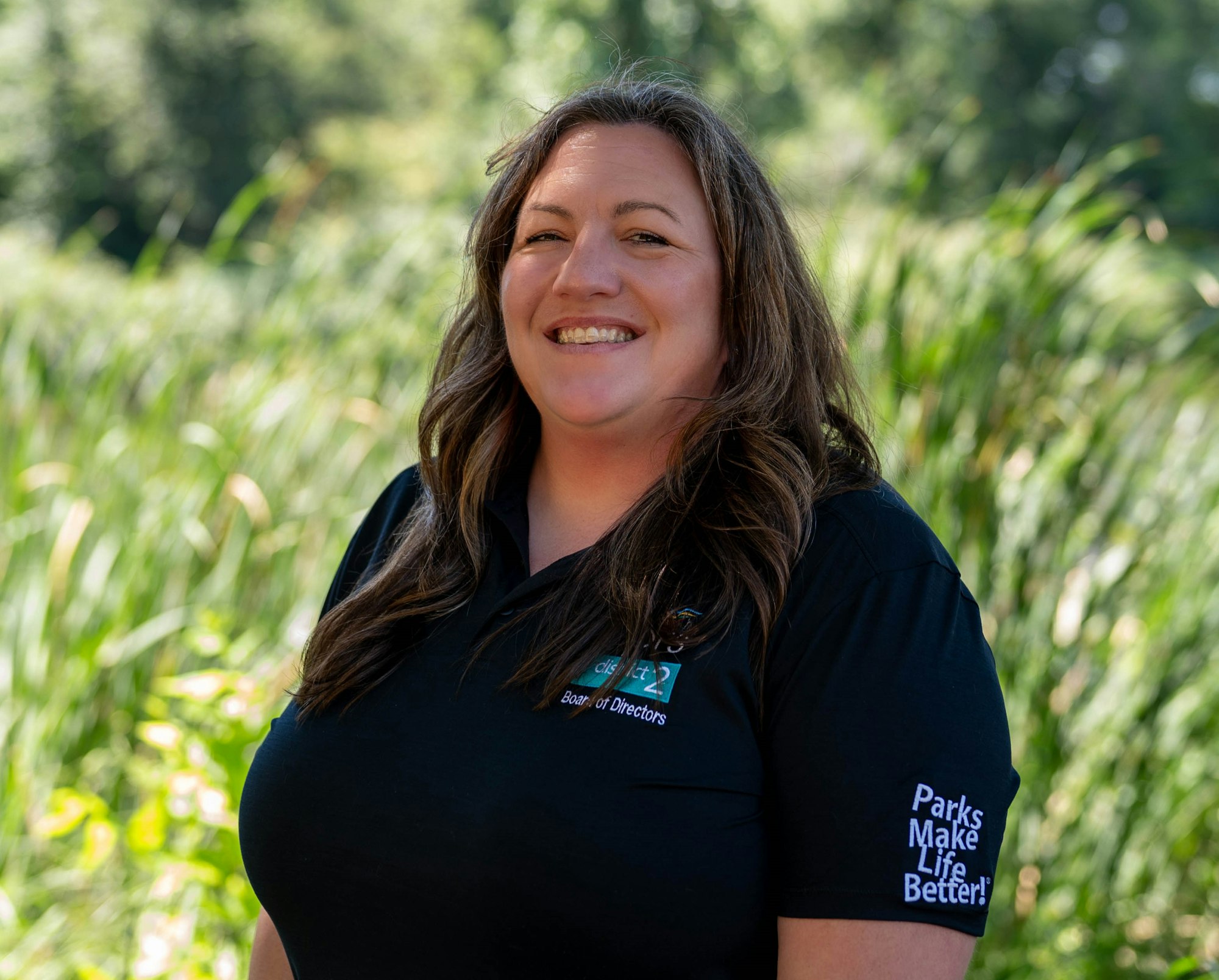 A person smiling outdoors, wearing a black shirt with "Board of Directors" and "Parks Make Life Better!" text.