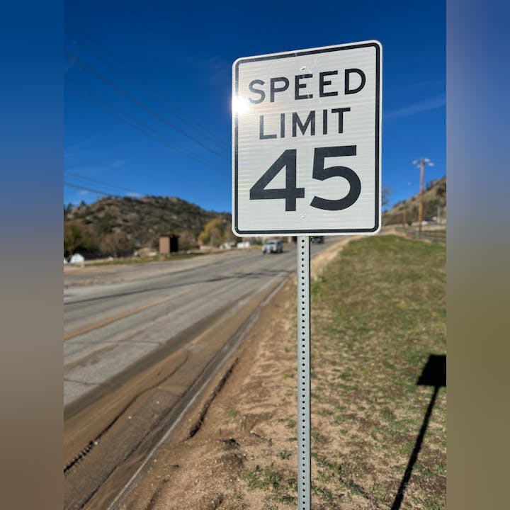 A speed limit sign indicating a maximum speed of 45 mph along a road, with hills and a clear blue sky in the background.