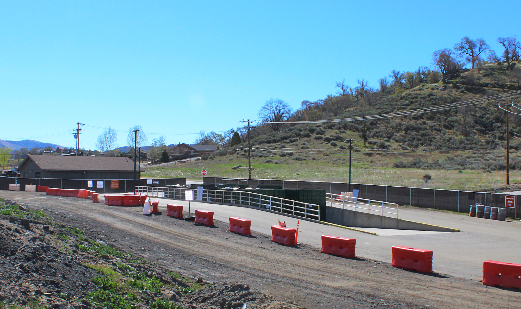 Outdoor facility with orange barriers, a building, fence, and ramp. Hills in the background, clear blue sky.