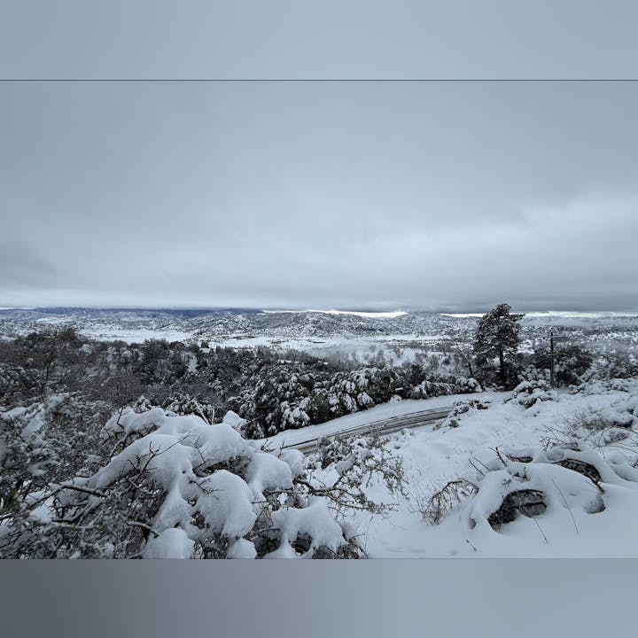 A snowy landscape with trees and mountains under a cloudy sky, showing a peaceful winter scenery.
