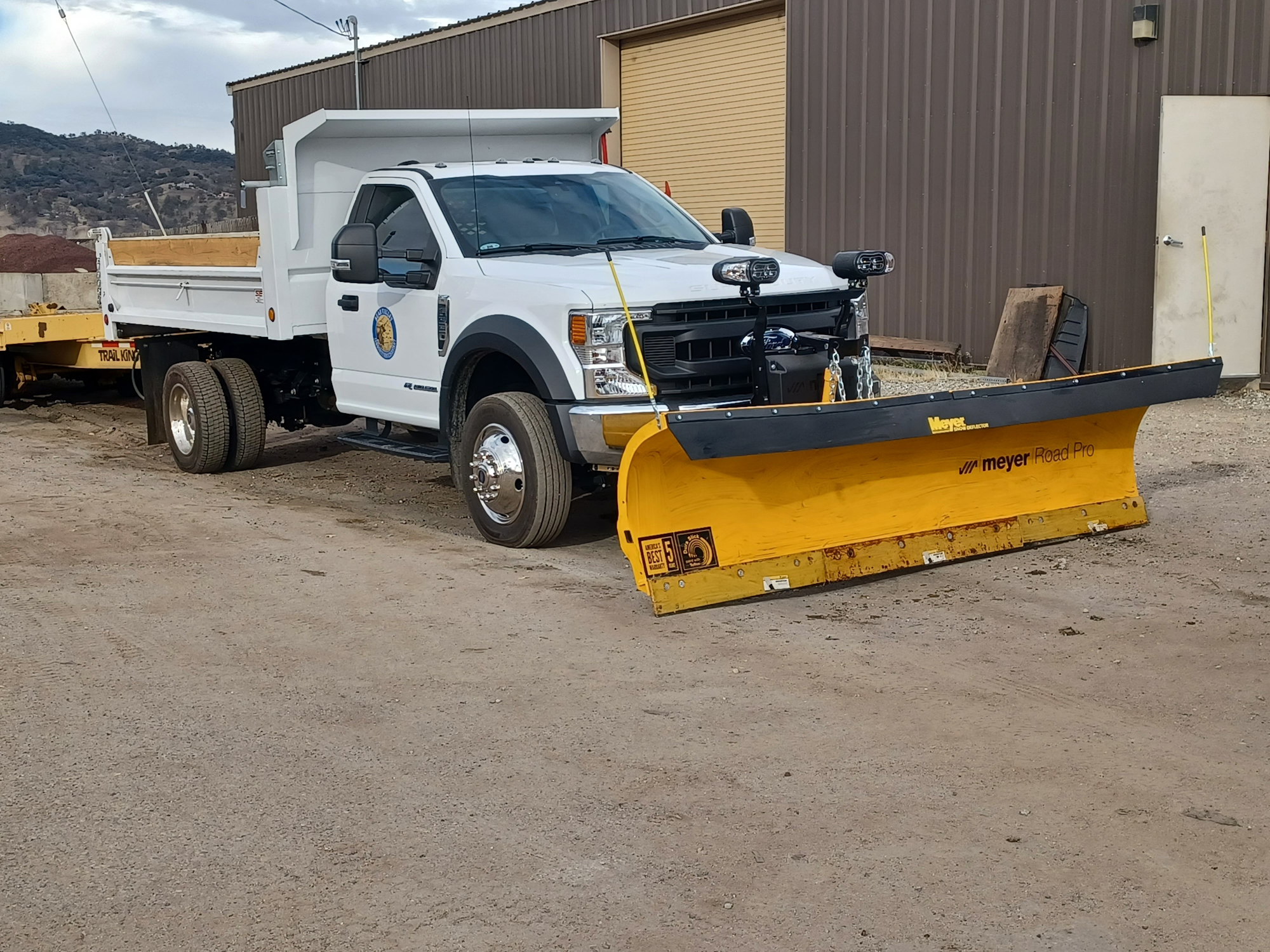 A white truck with a yellow snow plow attachment, parked next to a building.