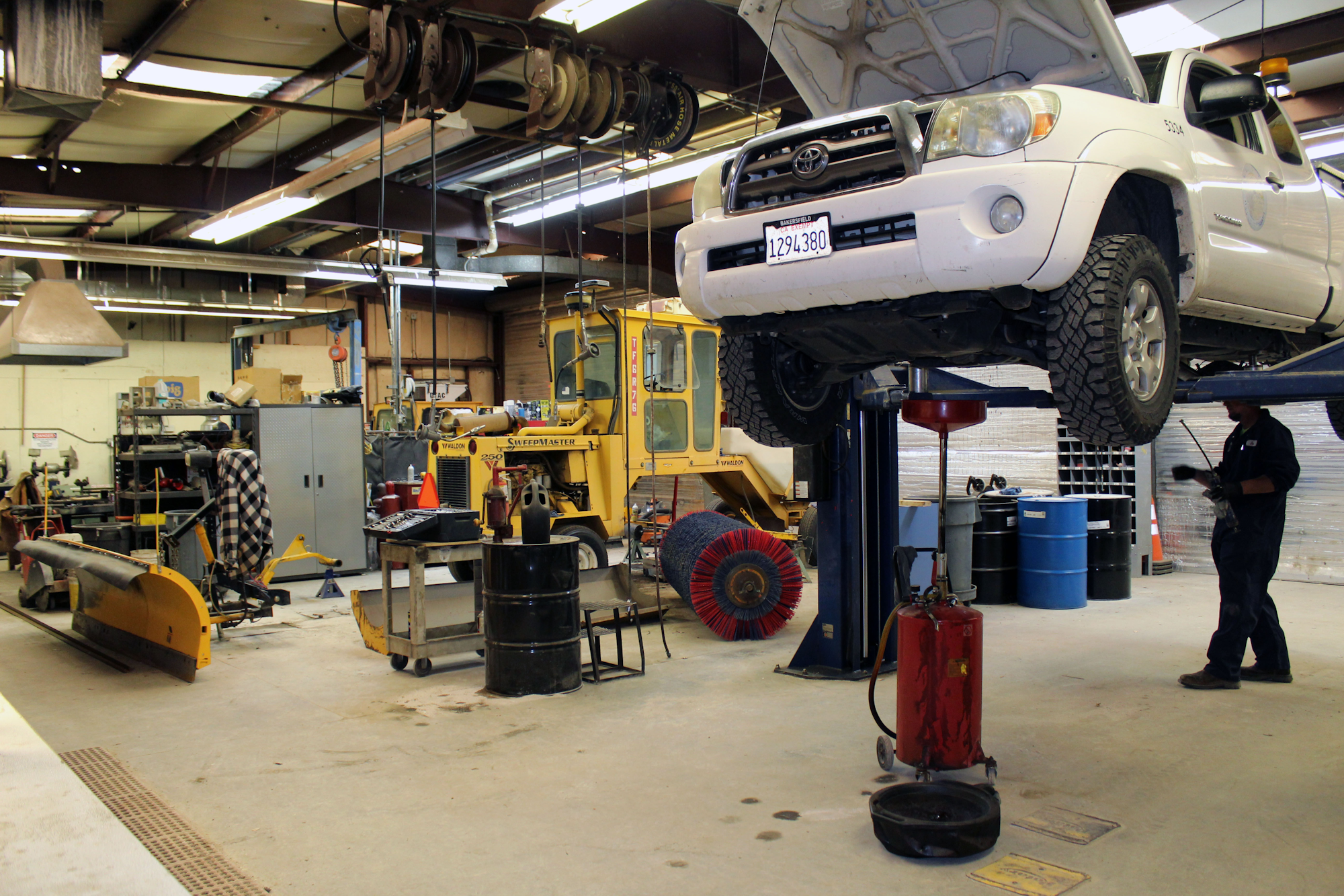 The image shows a vehicle maintenance shop with a lifted truck, various tools, equipment, and a technician working.