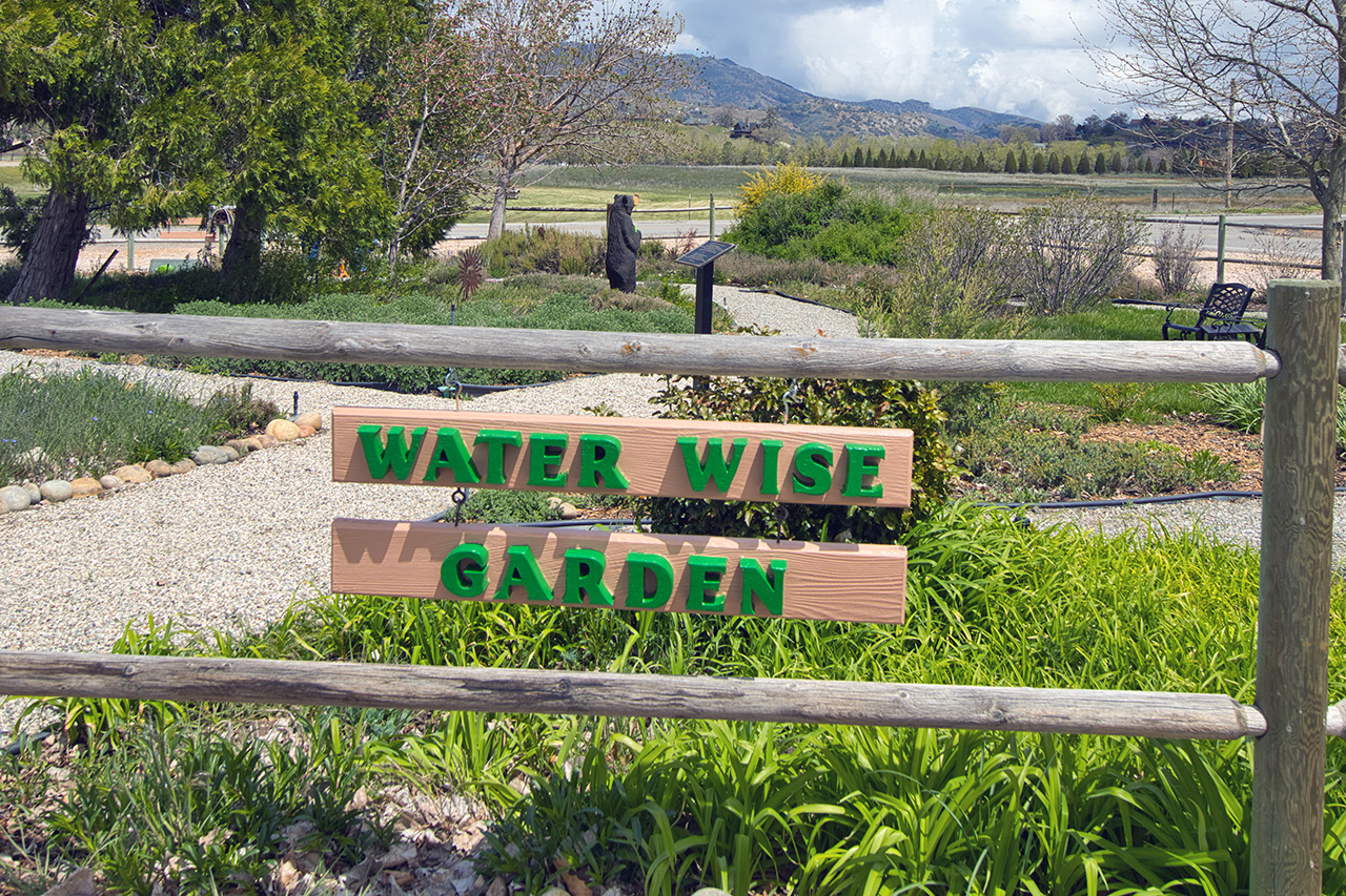 Sign reading “Water Wise Garden” with greenery and scenic mountains in the background.