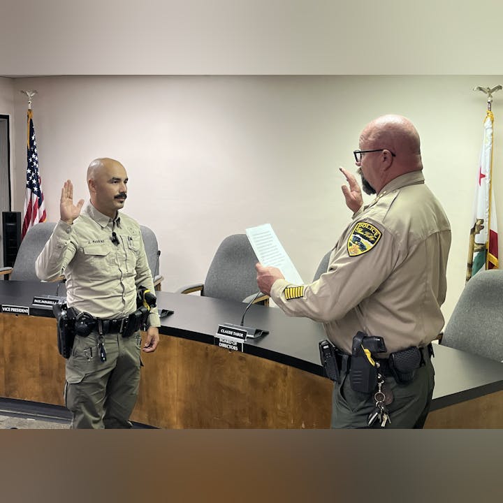 Two uniformed officers are swearing in during a formal ceremony in a meeting room.