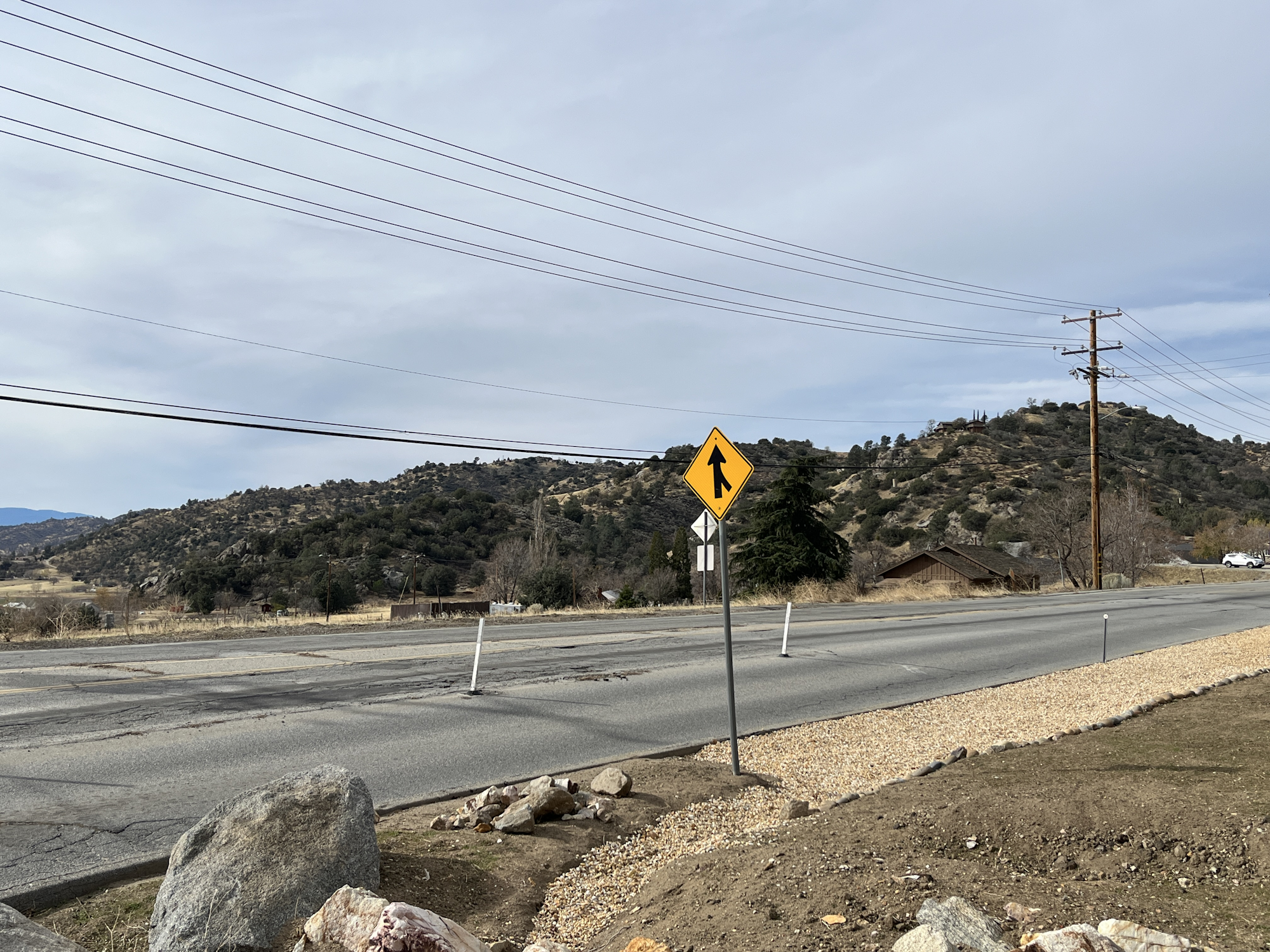 Road with a merge sign, power lines, and hills in the background.