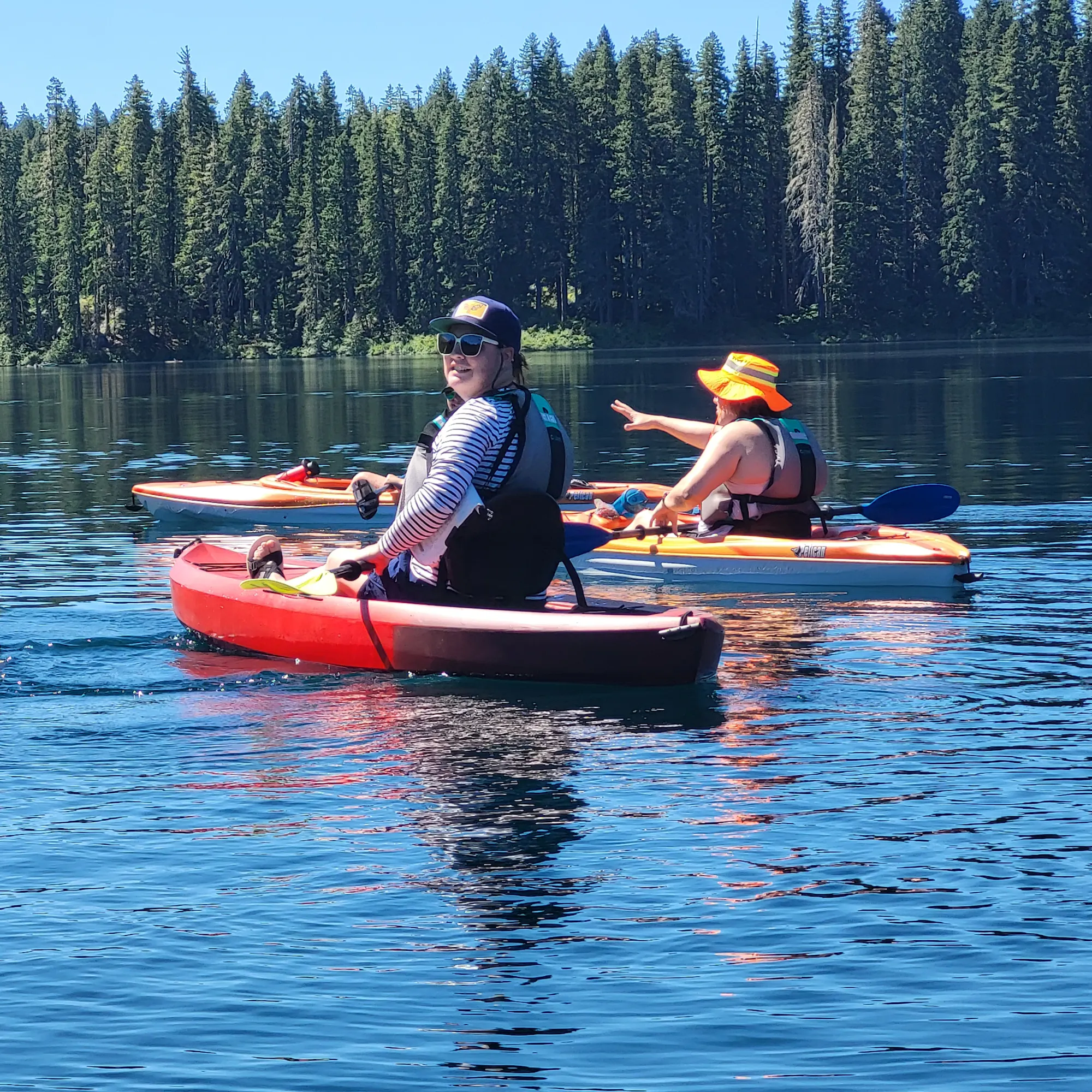 A group of people kayaking on a calm lake surrounded by trees on a sunny day.