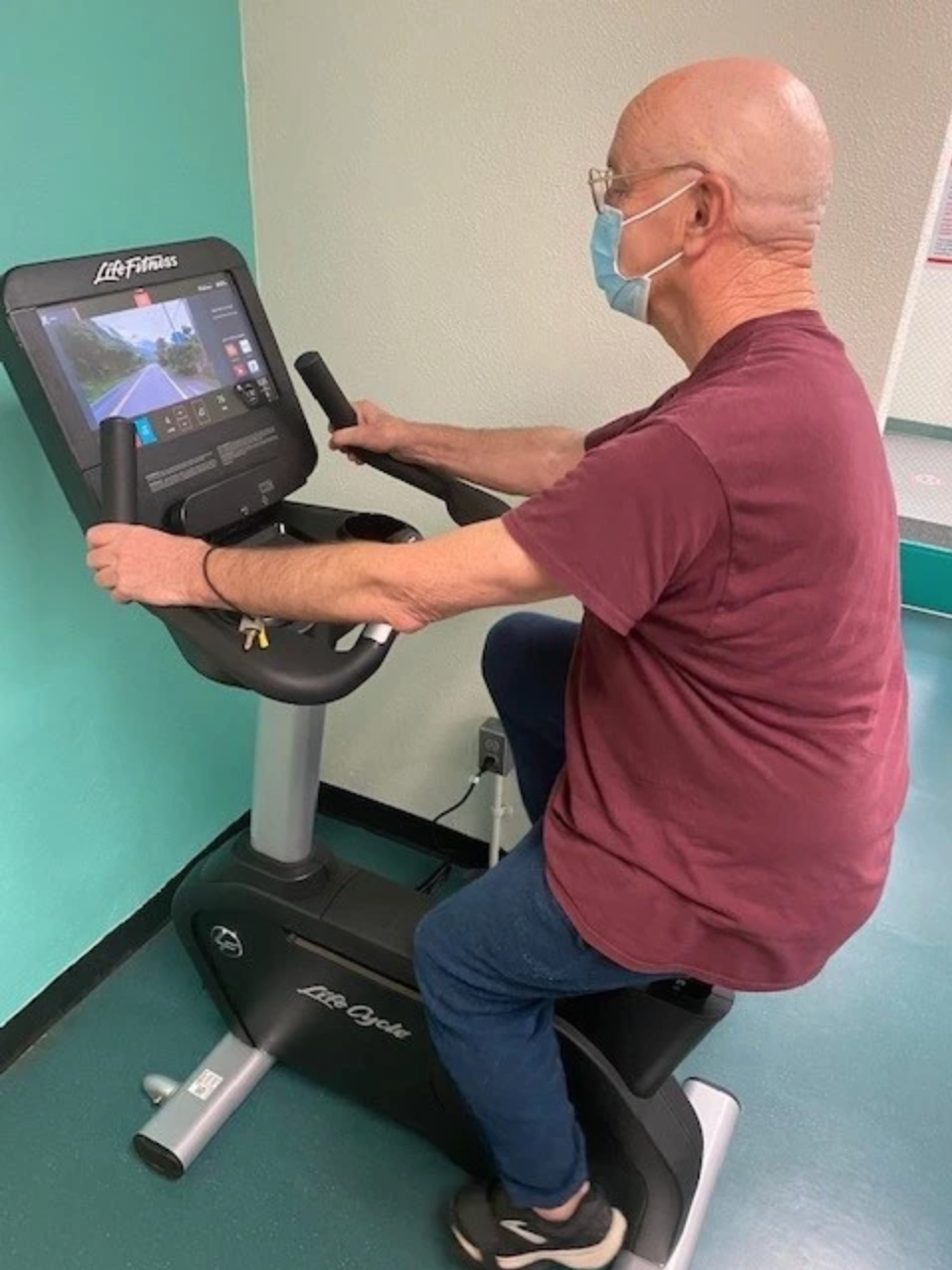 A person exercising on a stationary bike wearing a mask.