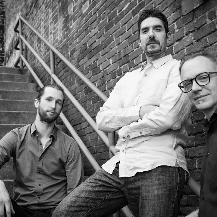 Three men posed on outdoor stairs, leaning against a brick wall. Black and white photo.