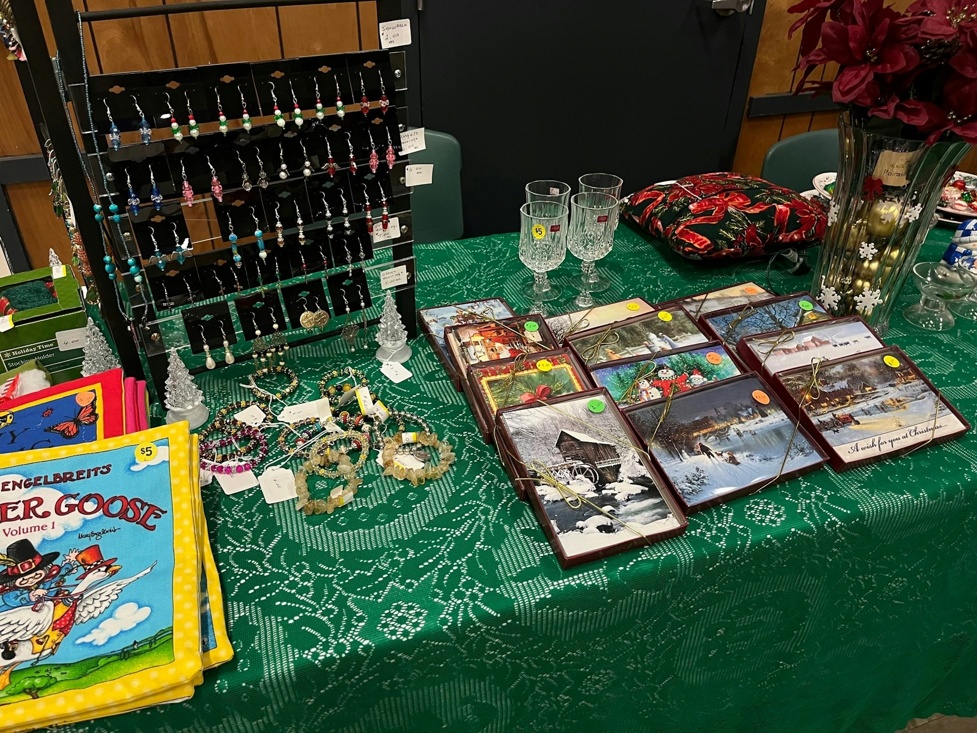 A table with assorted items like jewelry, books, Christmas cards, glasses, and decorative pieces displayed for sale.