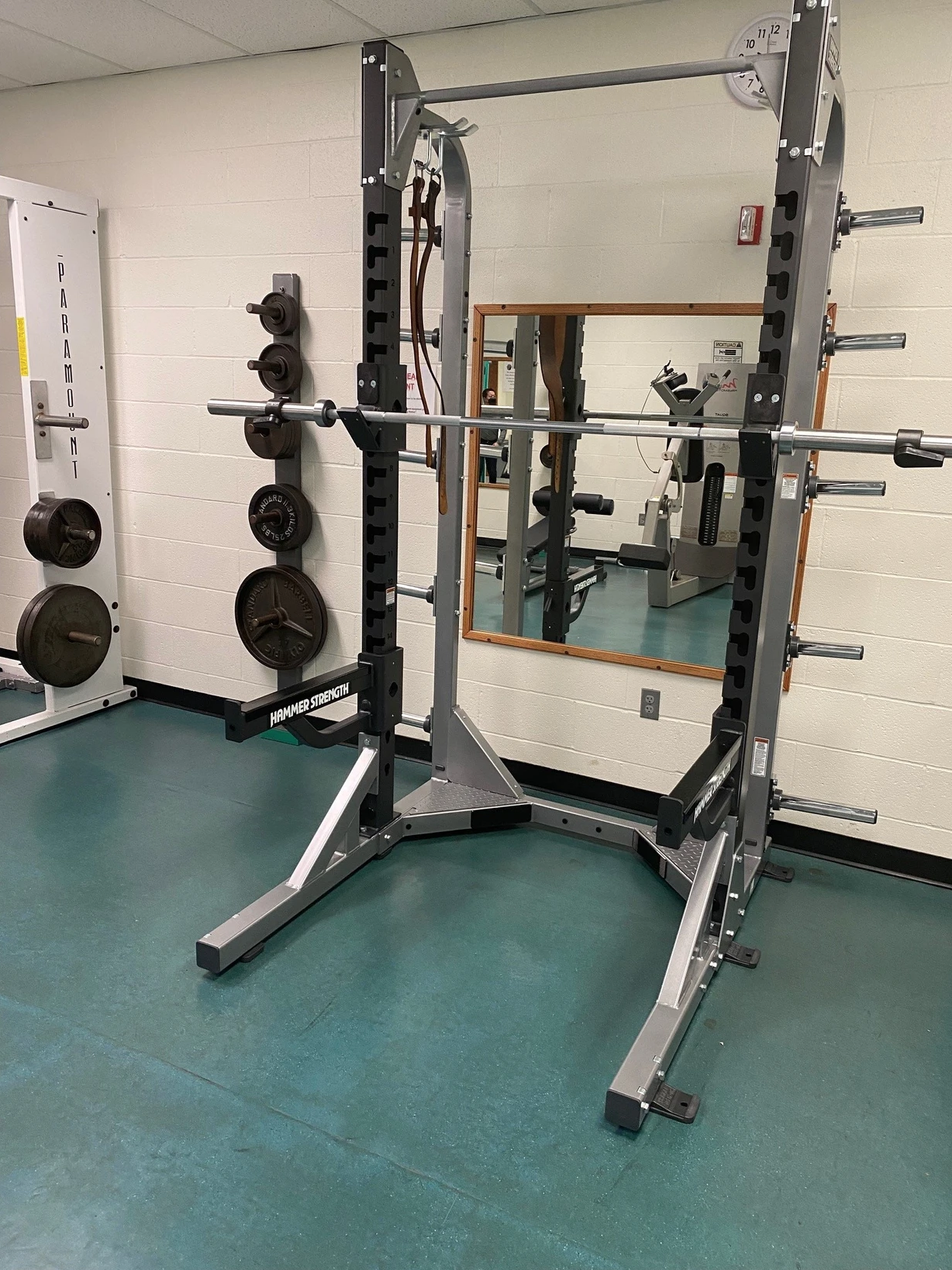 A squat rack with a barbell in a gym, surrounded by weight plates and mirrors.