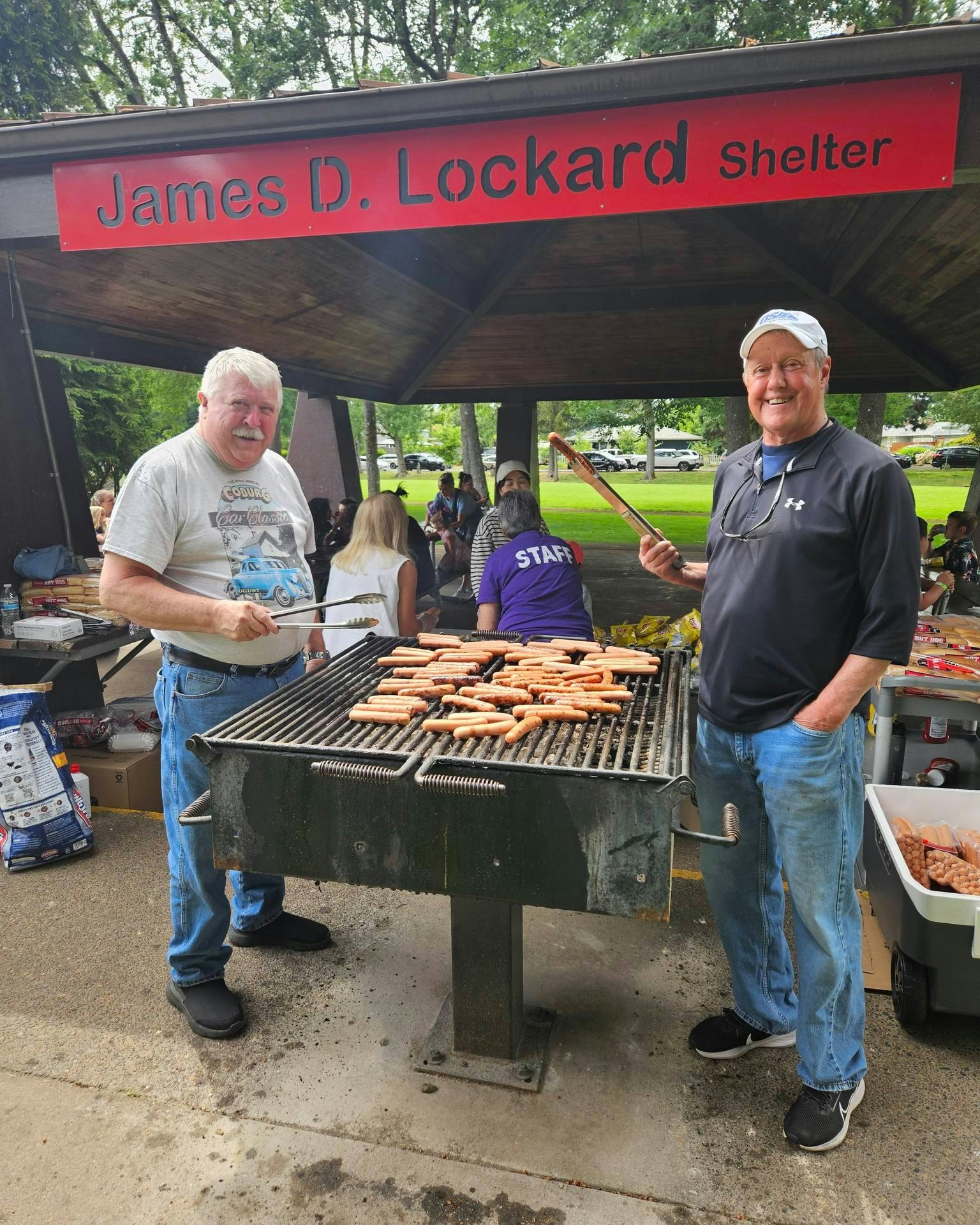 Two people grilling hot dogs at a park shelter named "James D. Lockard Shelter".