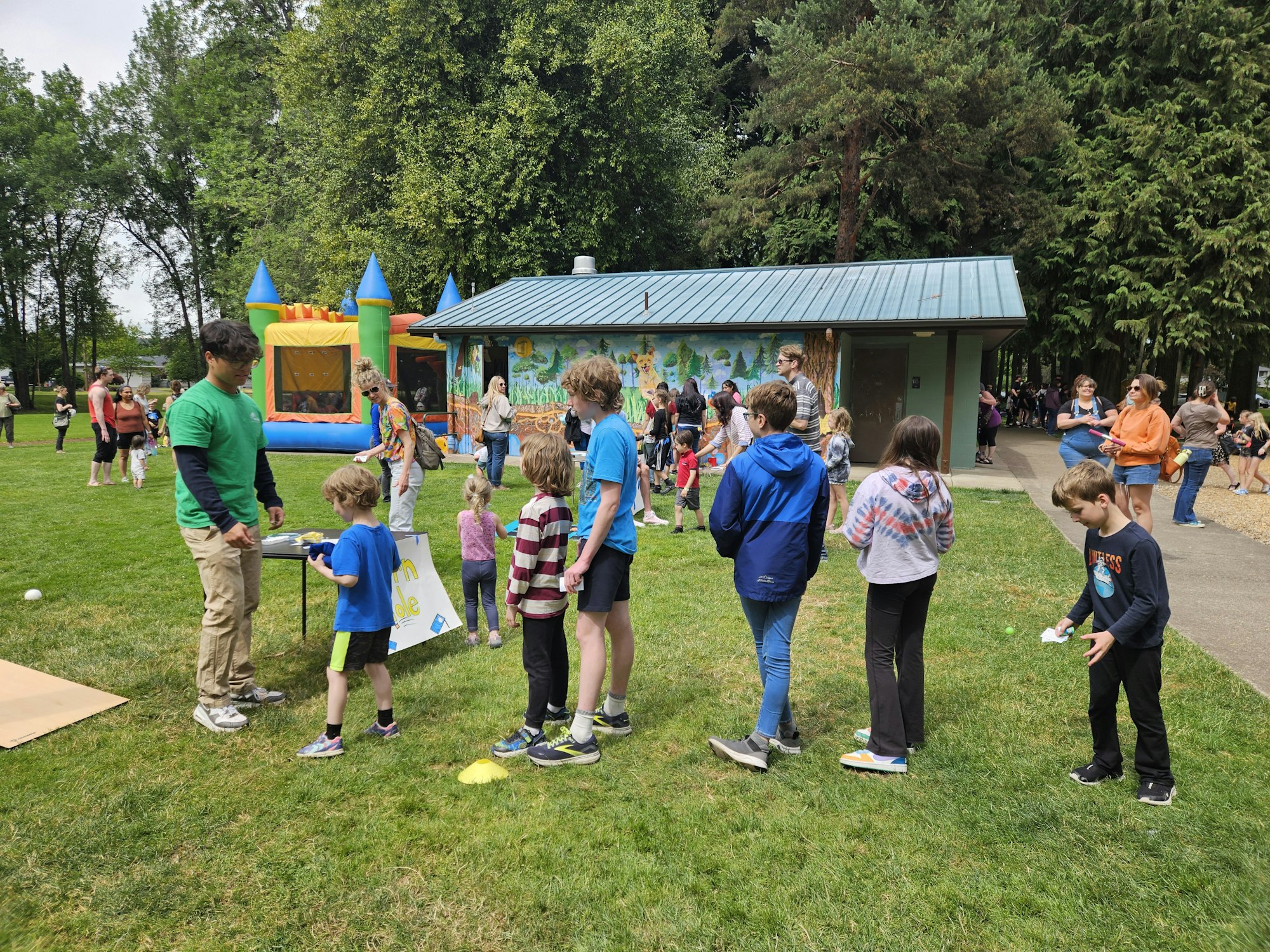 People at an outdoor event with a bounce house, mural, and grassy area.