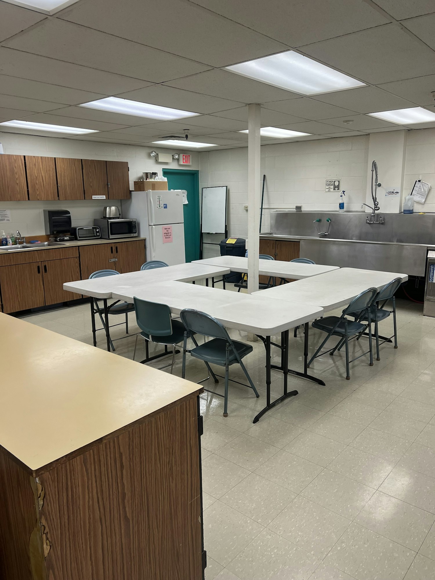 Classroom with tables, chairs, cabinets, a sink, and kitchen appliances.