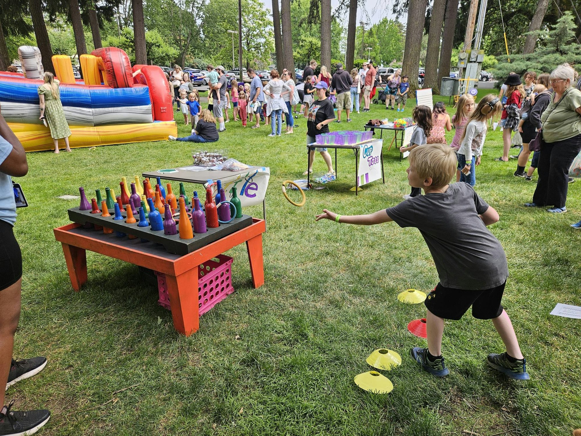 A lively outdoor event with children playing games, an inflatable bounce house, and colorful activities displayed on tables.
