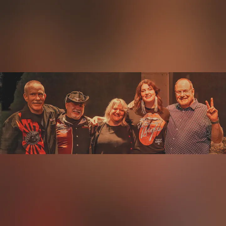 Five people posing together, three men and two women, smiling and standing arm in arm.
