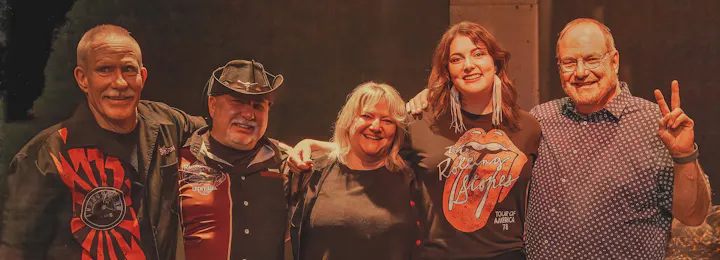 Five people posing together, three men and two women, smiling and standing arm in arm.