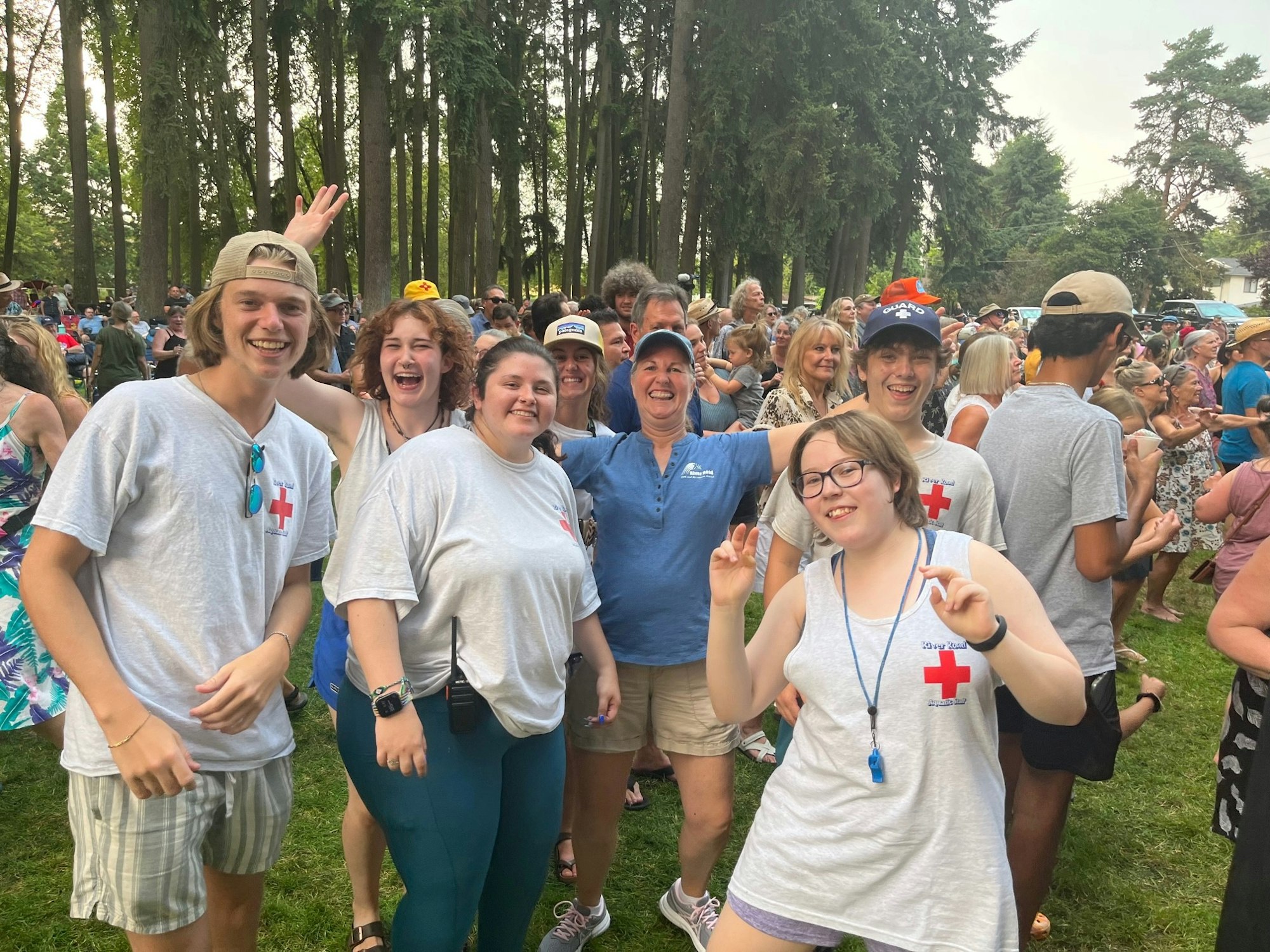 A group of people smiling at an outdoor event, with trees in the background.