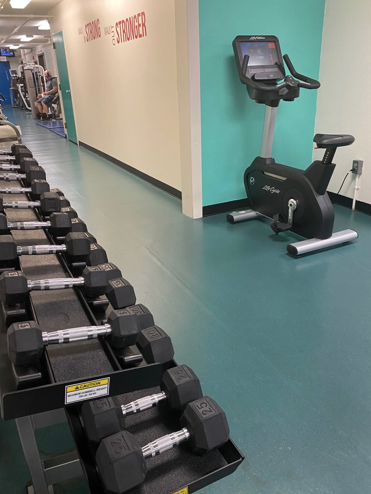 A gym with dumbbells in the foreground and a stationary bike in the background, with motivational text on the wall.
