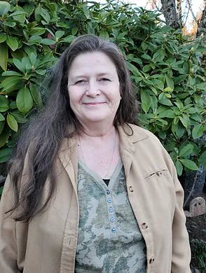 A smiling woman standing in front of green foliage.