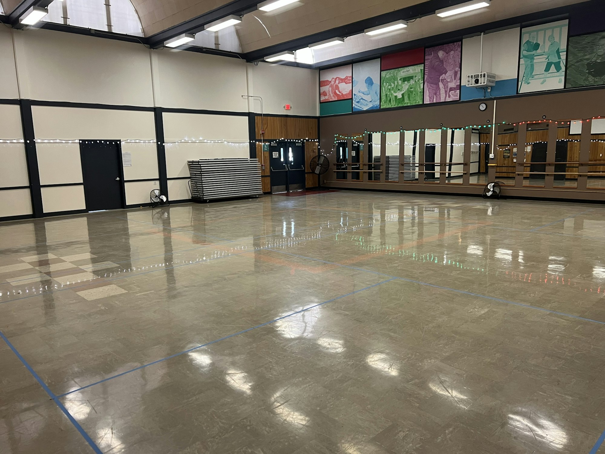 An empty dance studio with mirrors, artwork, and lights on the wall.