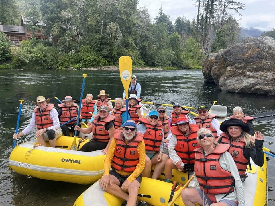 Group of smiling people in life jackets on rafts, holding paddles, with nature in the background.