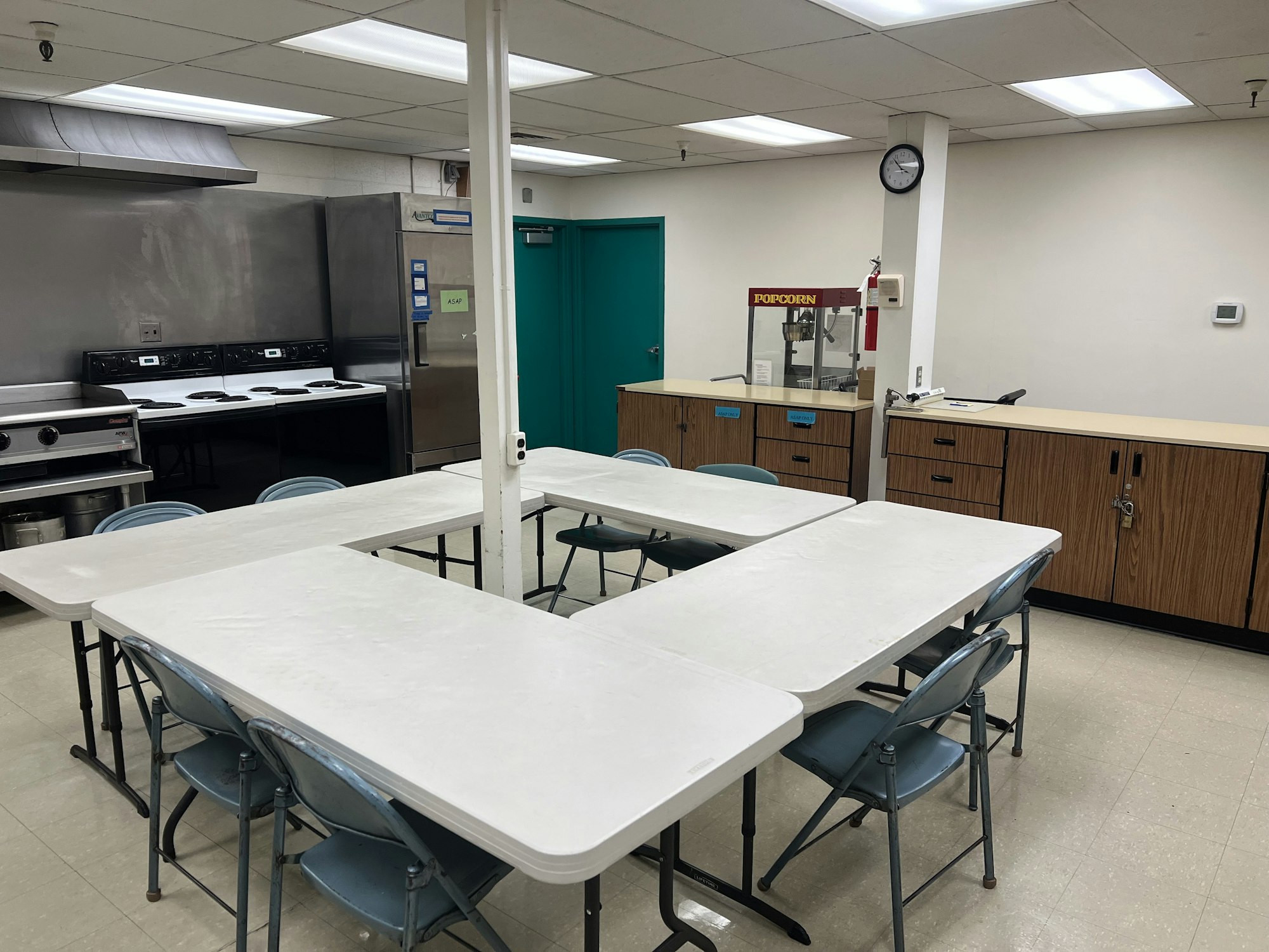 A kitchen with stoves, a popcorn machine, tables, and chairs, arranged in a U-shape.