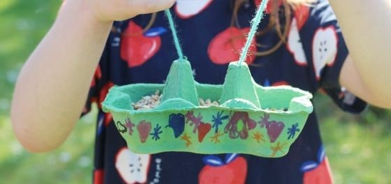A child holding a decorated egg carton bird feeder with seeds.