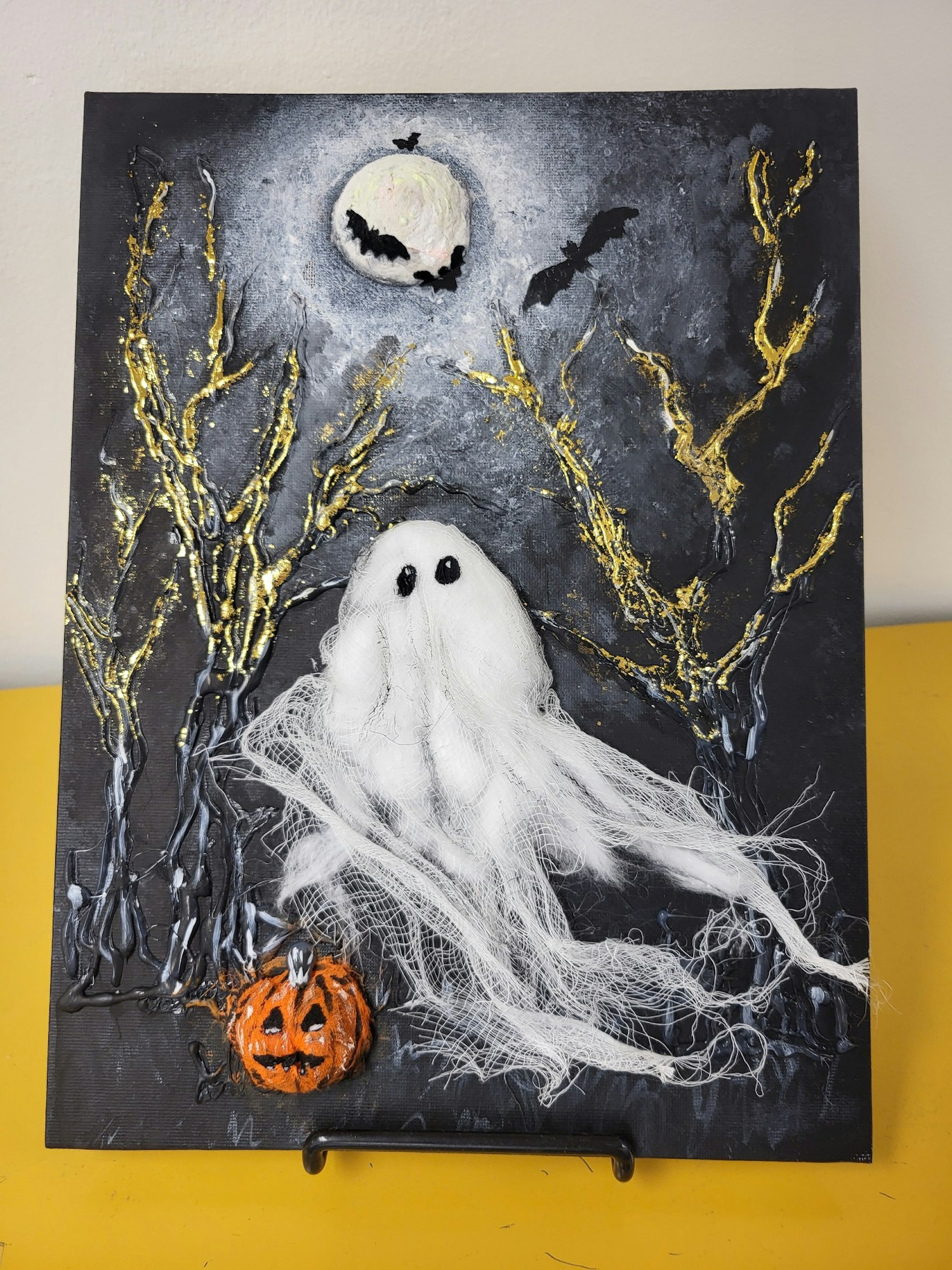A textured Halloween painting with a ghost, bats, moon, creepy tree branches, and a jack-o'-lantern.