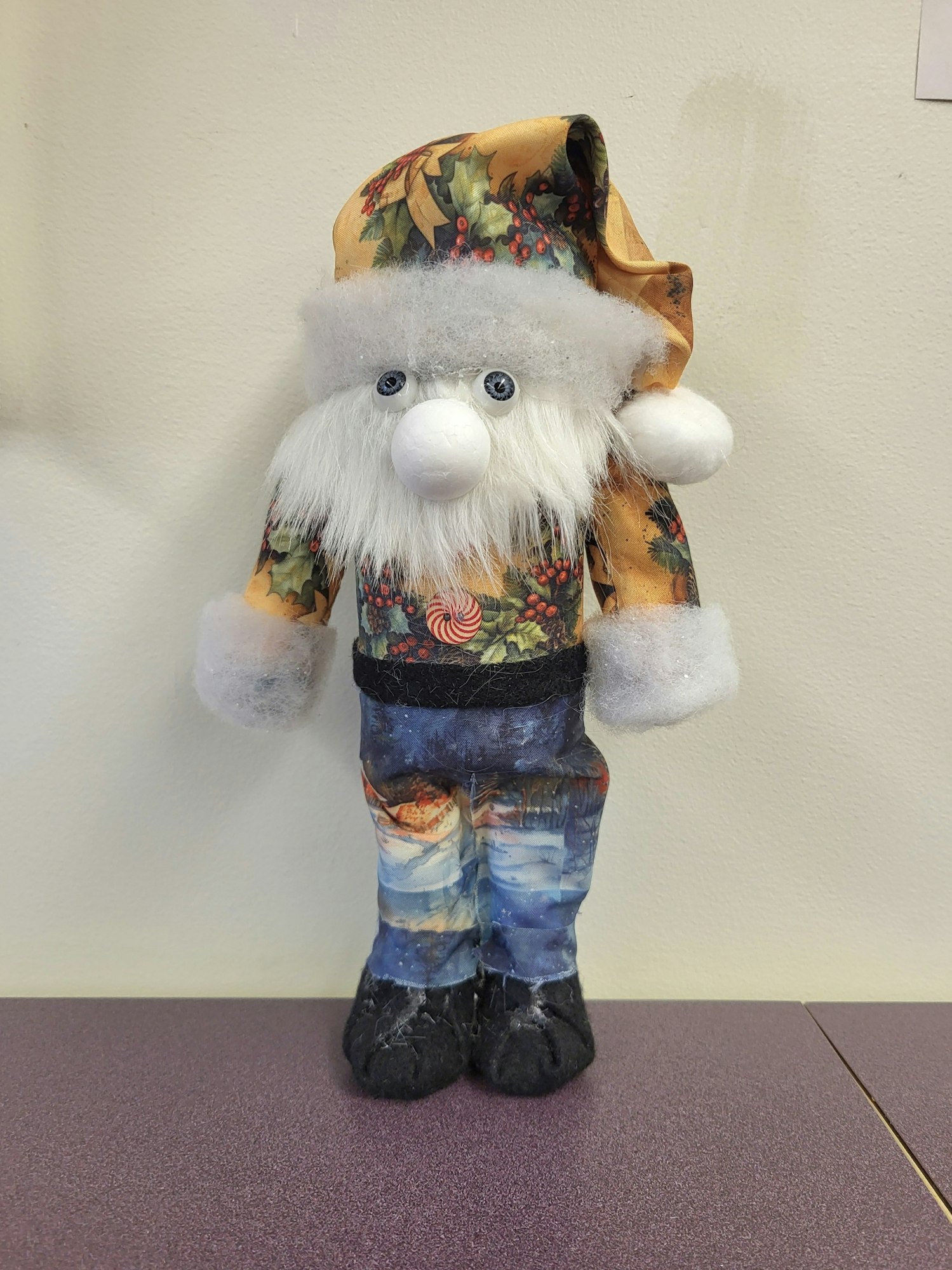 A whimsical doll with a fluffy beard, wearing a festive outfit and hat, featuring holiday patterns and a cheerful expression.