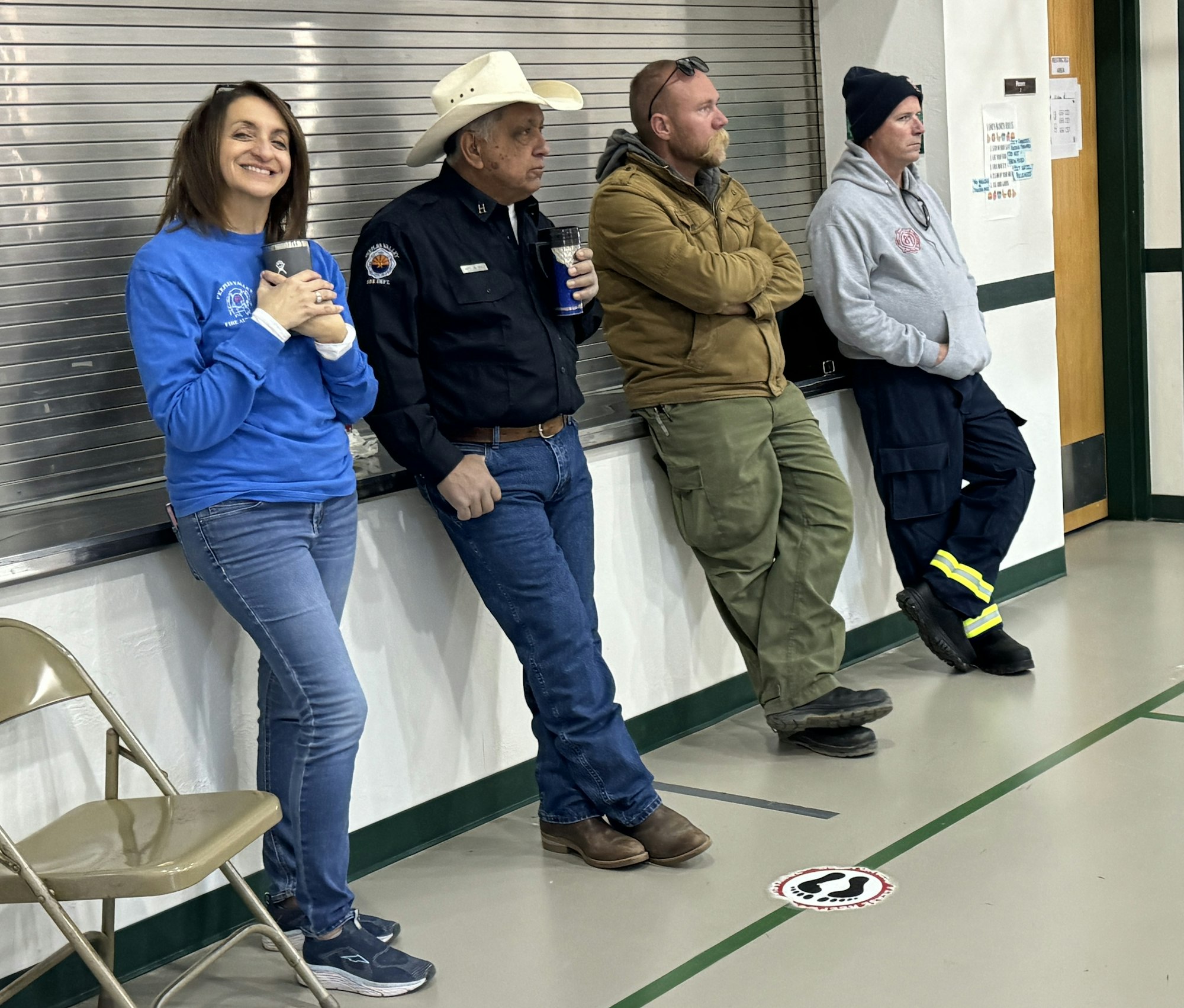 Four people standing by a wall, casually dressed, indoors.