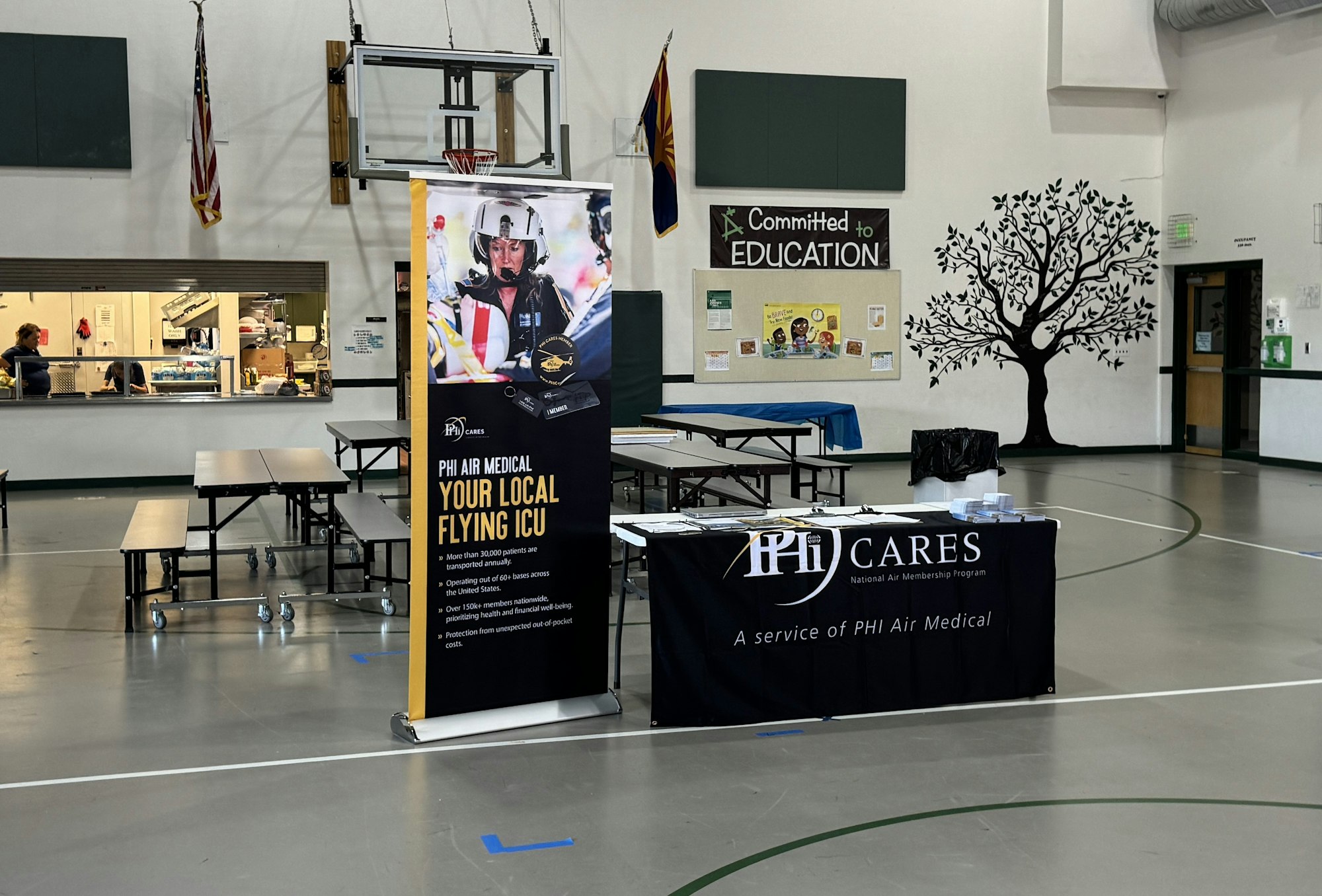 A gym with a PHI Air Medical information booth, tables, and an "Committed to Education" bulletin board.
